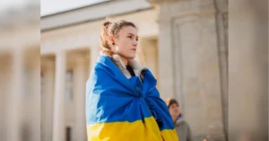 Молода жінка з прапором України на плечах біля будівлі з колонами