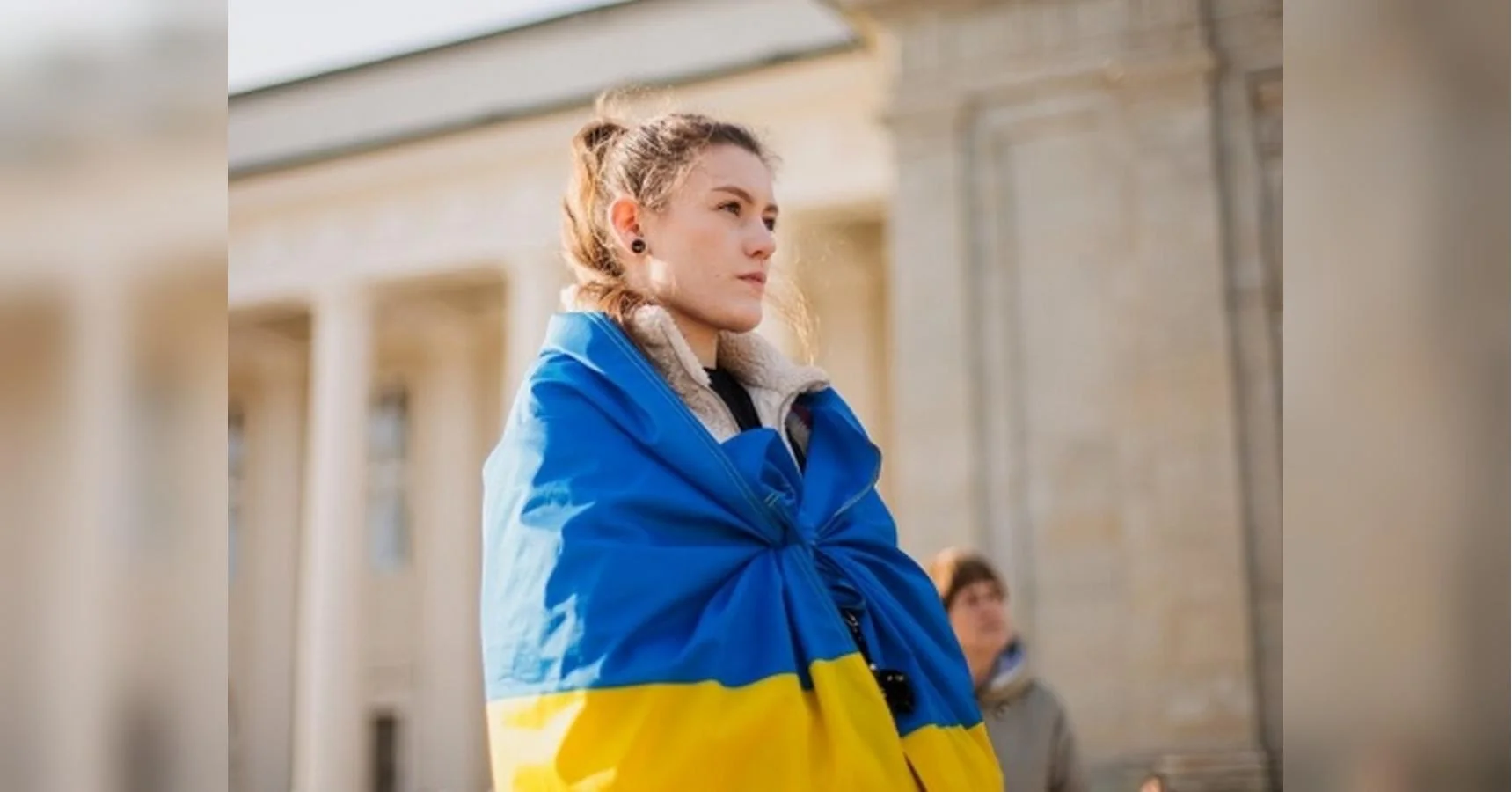 Молода жінка з прапором України на плечах біля будівлі з колонами